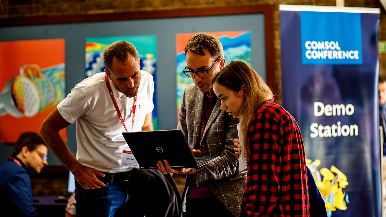 Drie conferentiedeelnemers kijken samen naar een laptop bij een COMSOL Conferentie demo station.