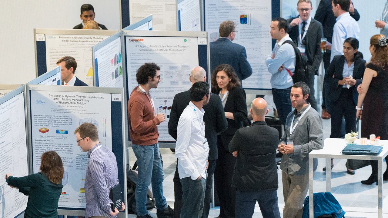 Twee deelnemers aan de COMSOL Conference in de tentoonstellingshal, waar één van hen zijn werk presenteert.